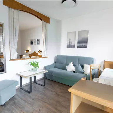 A modern living room with a cozy sofa and a coffee table. Pictures hang on the wall and a mirror reflects the space.