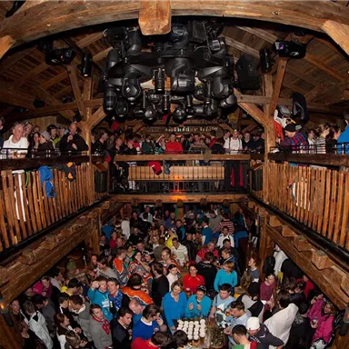 A lively interior with many people enjoying a celebration. Wooden details and a high ceiling create a cozy atmosphere.