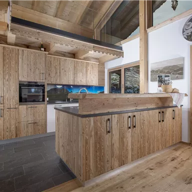 Moderne Küche aus Holz mit einer klaren Arbeitsfläche und einem eleganten Design. Große Fenster bieten viel Licht und einen Blick auf die Natur.