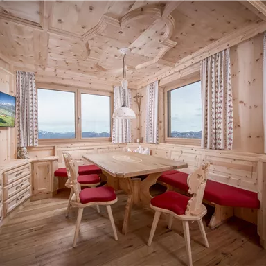 Eine gemütliche Holzküche mit einem großen Tisch und roten Stühlen. Die Fenster bieten einen wunderschönen Blick auf die Berge.