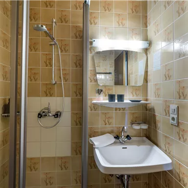 Ein kleines Badezimmer mit Dusche und Waschbecken. Die Wände sind mit beigem Fliesenmuster dekoriert.
