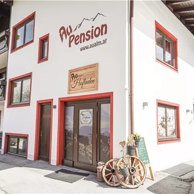 Eine gemütliche Pension mit rotem und weißem Außenanstrich. Im Vordergrund befindet sich ein rustikales Schild und eine Wagenrad-Dekoration.