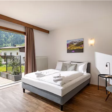 Ein modernes Schlafzimmer mit einem Doppelbett und Blick auf die Berge. Es gibt einen Balkon mit Sitzgelegenheiten und eine gemütliche Atmosphäre.