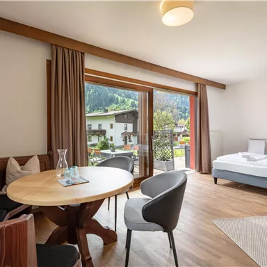 Ein modernes Zimmer mit einem Doppelbett und einem Essbereich. Große Fenster ermöglichen einen Blick auf die Natur außerhalb.