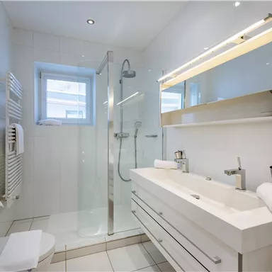 A modern bathroom with a bright shower and an elegant sink. The walls are kept in white, creating a clean and timeless look.