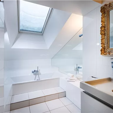 A modern bathroom with a large window and a bathtub. The walls and tiles are in light colors, making the space feel open and inviting.