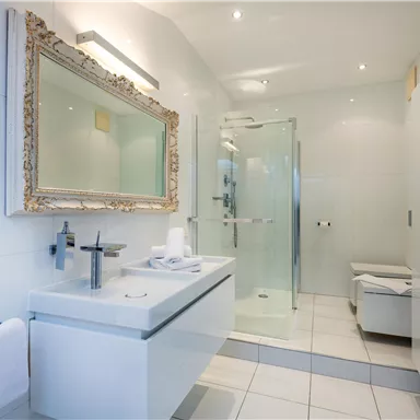 A modern bathroom with elegant tiles and a glass shower. The large mirror adds extra shine to the space.