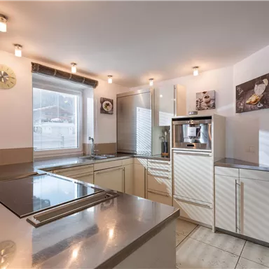 A modern kitchen with bright furniture and gray surfaces. Large windows provide plenty of daylight.