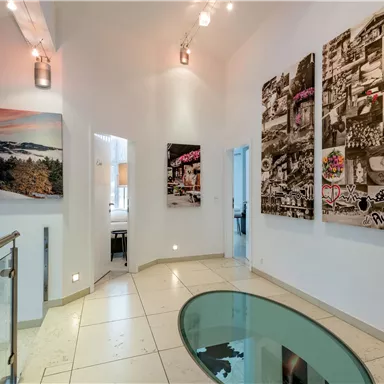 A modern hallway with bright walls and elegant artworks. The floor is made of glossy tiles and there is a stylish glass tabletop.