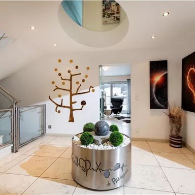 A modern entrance area with an elegant staircase and stylish wall decorations. In the center, there is a round table with plants and a decorative element.