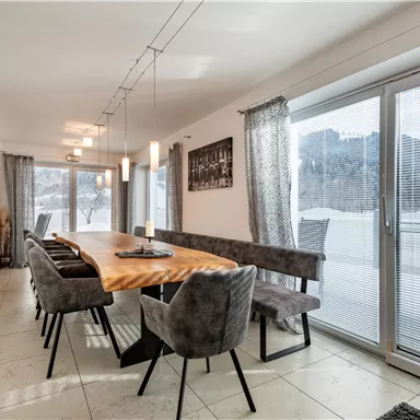 An elegant dining area with a long wooden table and upholstered chairs. Large windows provide a view of the wintry landscape.