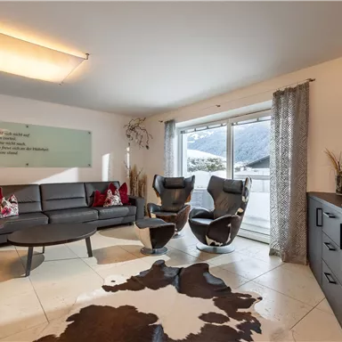 A modern living room with a stylish sofa and two comfortable armchairs. Large windows offer a view of the surrounding landscape.