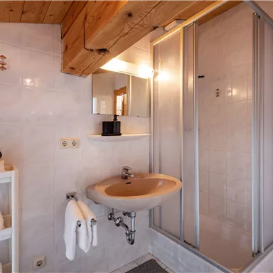 A modern bathroom with a shower and a sink. There are fresh towels and a cozy wooden ceiling.
