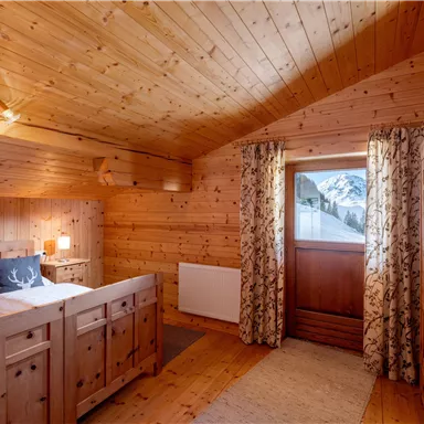 A cozy wooden bedroom with a large window that offers a view of the mountains. The decor is warm and inviting, perfect for a relaxing stay.
