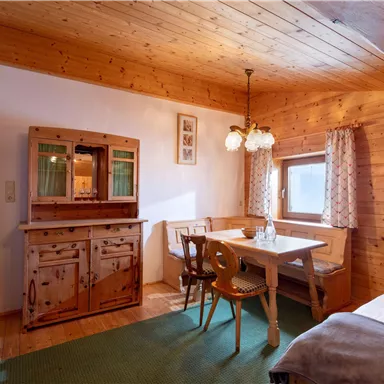 A cozy room with wooden paneling, a dining table, and chairs. In the background, there is a beautiful sideboard and a window that lets in plenty of light.