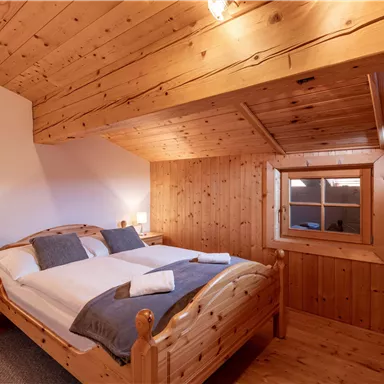 A cozy bedroom with a wooden frame bed and two nightstands. The walls and ceiling are also made of wood, with a small window that lets in natural light.