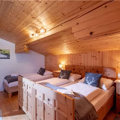 A cozy bedroom with wooden paneling and two beds. The warm light sources create an inviting atmosphere.