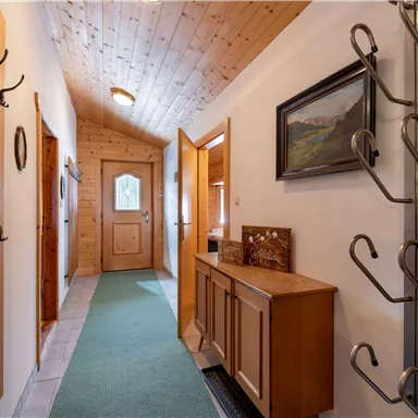 A bright hallway with wooden ceilings and a carpet. Coat hooks hang on the walls and a dresser is located next to the door.
