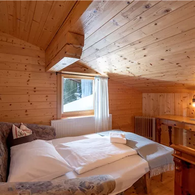 A cozy bedroom with wood paneling and a double bed. Daylight enters through the window, and the room feels warm and inviting.