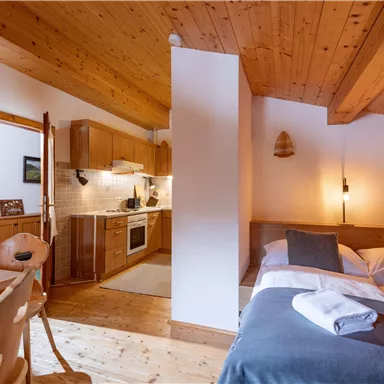 A cozy room with wooden ceilings and a modern kitchenette. The sleeping area is bright and inviting, perfect for relaxing.