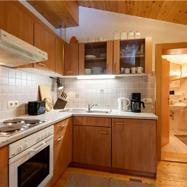 A modern kitchen with wooden cabinets and a bright countertop. In the background, access to a bathroom is visible.