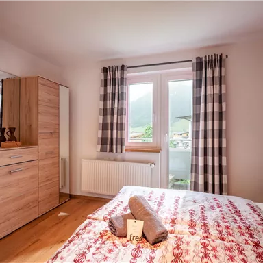 A cozy bedroom with a large window and a view of the mountains. The decor is modern with wood and red elements.