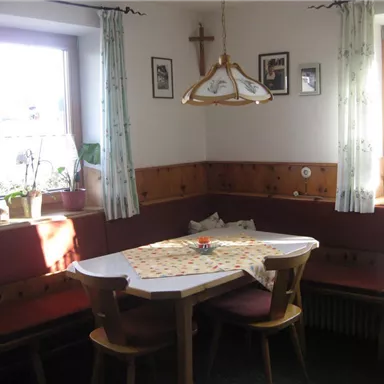 A cozy dining area with a bench and a table. The walls are clad in wood, and there are some plants and pictures.