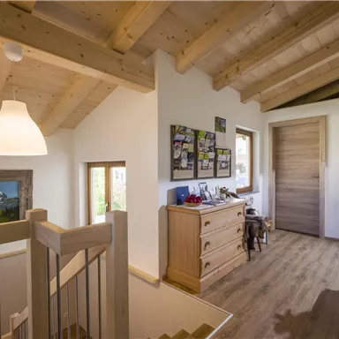 Ein heller Flur mit Holzdecke und großen Fenstern. An der Wand hängen Bilder, und es steht ein Möbelstück mit verschiedenen Gegenständen.