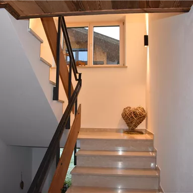 A bright hallway with a staircase and wooden details. At the end of the staircase stands a decorative heart made of natural materials.