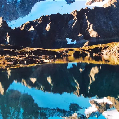 Eine wunderschöne Berglandschaft mit schneebedeckten Gipfeln und einem klaren See. Die Berge spiegeln sich ruhig im Wasser.