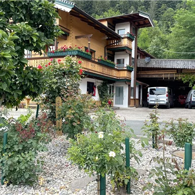A cozy house with balconies and flower gardens. Parking spaces are also visible, surrounded by green plants.