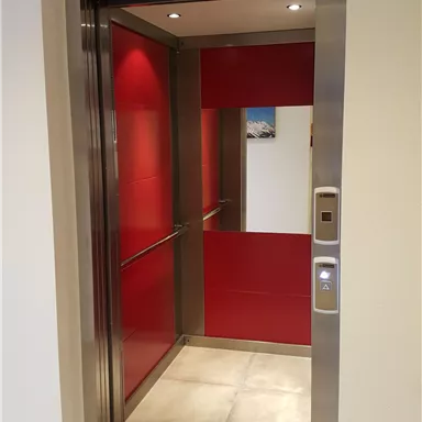 Ein moderner Aufzug mit roten Wänden und glänzenden Metallverkleidungen. Der Aufzug ist offen und bereit für Passagiere.