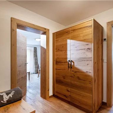 A modern-designed hallway with wooden furniture and an open entrance to another room. Bright walls and large windows provide plenty of light.