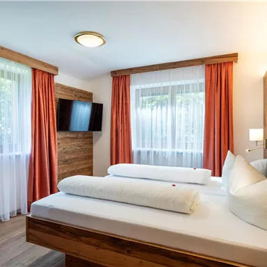 A cozy bedroom with two beds and modern wooden details. Large windows let in plenty of light and create a friendly atmosphere.