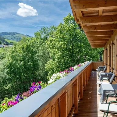 A beautiful balcony with wooden cladding and a view of green trees and mountains. Flowers adorn the railing and invite you to relax.