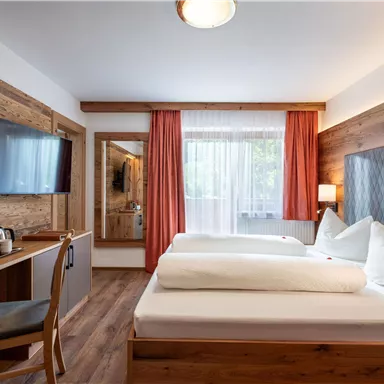A modern room with two beds and wooden details. The room is bright and inviting, with windows and a flat-screen TV.