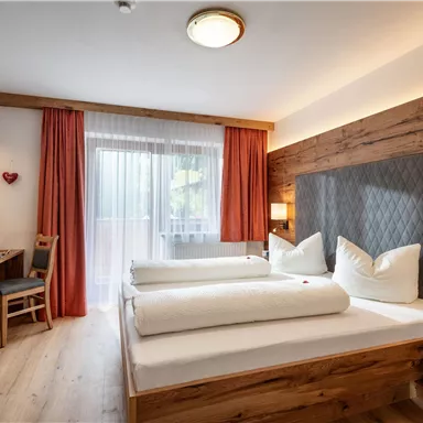 A modern hotel room with two beds and warm wooden elements. Large windows provide plenty of light and an inviting view outside.