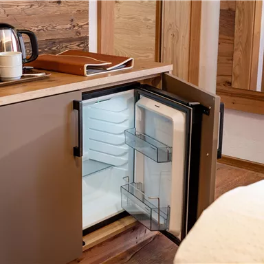 A small refrigerator in a cozy room. Next to the refrigerator is a teapot and a writing pad.