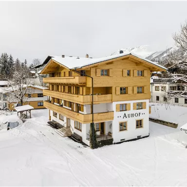 A wooden house in the snow with several floors. Surrounded by snowy trees and other buildings.