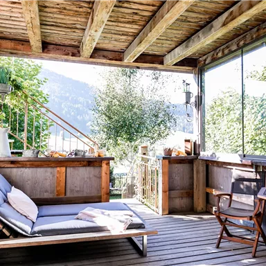 Ein einladender Balkon mit einem gemütlichen Liegestuhl und einem Tisch. Im Hintergrund sind Pflanzen und Bäume zu sehen, die eine entspannende Atmosphäre schaffen.