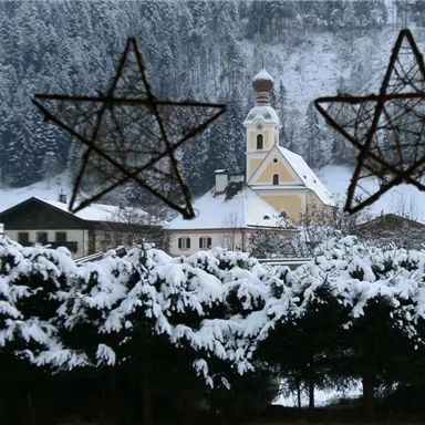 A snowy landscape with a charming village and a church in the background. The view is framed by two decorative stars.