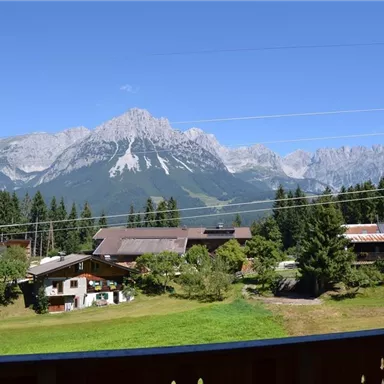 A picturesque mountain landscape with high peaks and green meadows. In the foreground, charming traditional houses can be seen.