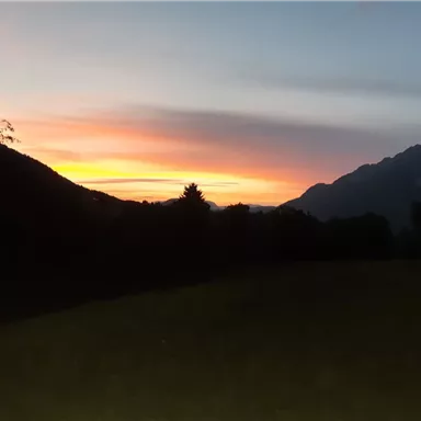 Ein atemberaubender Sonnenuntergang über den Bergen. Der Himmel ist in sanften Farben von Orange und Pink gefärbt.
