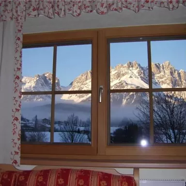 A view from a window of majestic mountains covered in snow. Outside, the sky is clear and the landscape appears peaceful.