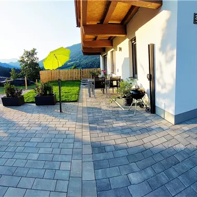 A cozy terrace with a table and a sunshade. In the background, green meadows and mountains can be seen.