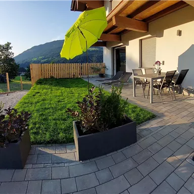 A beautiful garden seating area with a green lawn and modern planters. In the background, hills and a blue sky can be seen.