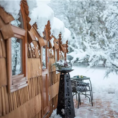 Eine gemütliche Holzhütte, umgeben von schneebedeckten Bäumen. Der Winterzauber ist spürbar durch die ruhige, verschneite Landschaft.