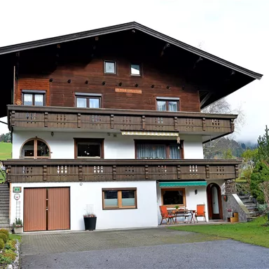 Ein traditionelles zweigeschossiges Haus mit Holzelementen und einem großen Balkon. Der Garten ist gepflegt und es gibt eine Terrasse mit Sitzgelegenheiten.