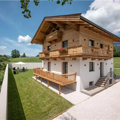 A charming wooden house with a balcony in a picturesque landscape. The surroundings are green and the mountains are visible in the background.