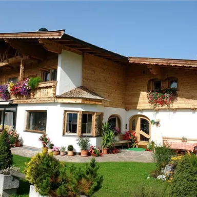 Ein schönes, traditionelles Haus mit Holzelementen und bunten Blumen. Es liegt in einer grünen Umgebung und hat eine einladende Atmosphäre.
